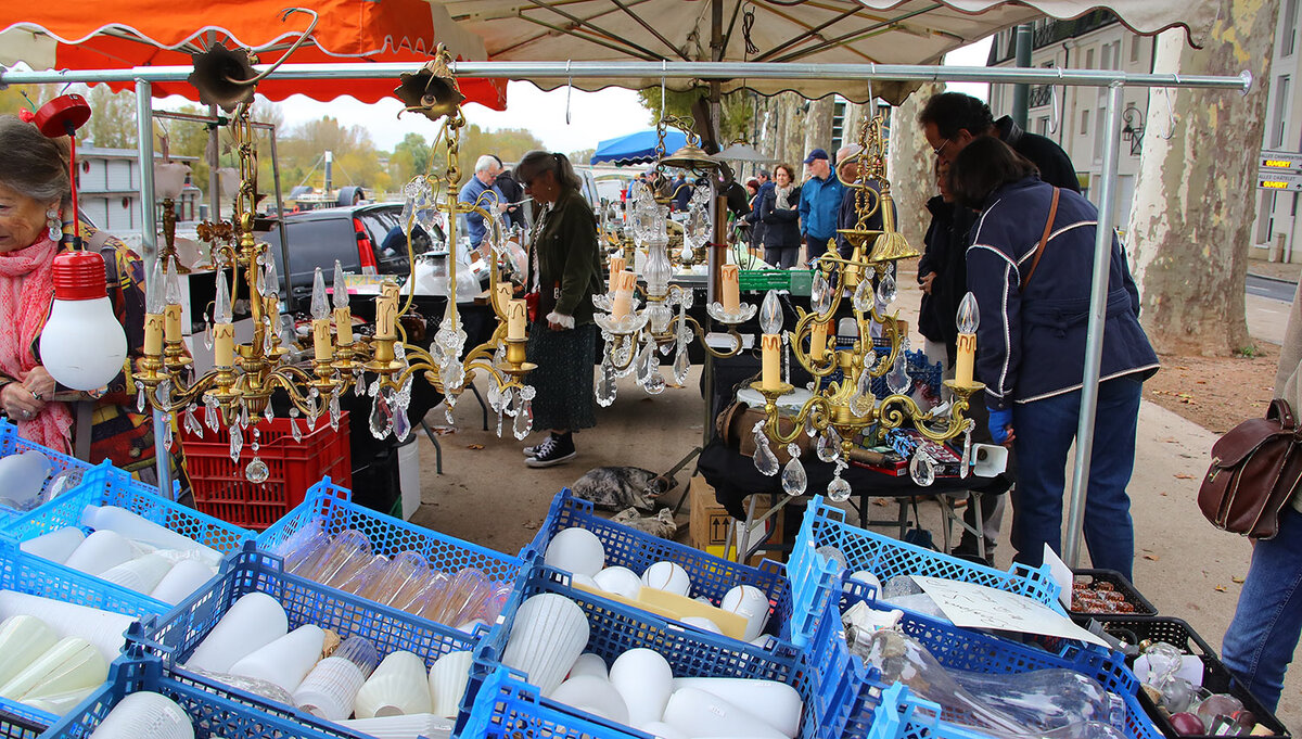 Stand de brocante en plein air, avec des lustres en laiton et cristal suspendus et des caisses d'abat-jour en verre, lors d'une brocante professionnelle sur les quais d'Orléans.