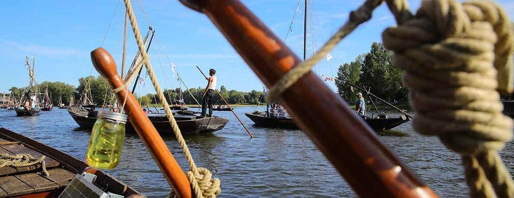 Bateaux traditionnels à voile sur la Loire lors du Festival de Loire à Orléans, avec mariniers en tenue d’époque naviguant sous un ciel bleu.