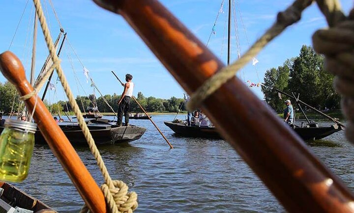 Bateaux traditionnels à voile sur la Loire lors du Festival de Loire à Orléans, avec mariniers en tenue d’époque naviguant sous un ciel bleu.