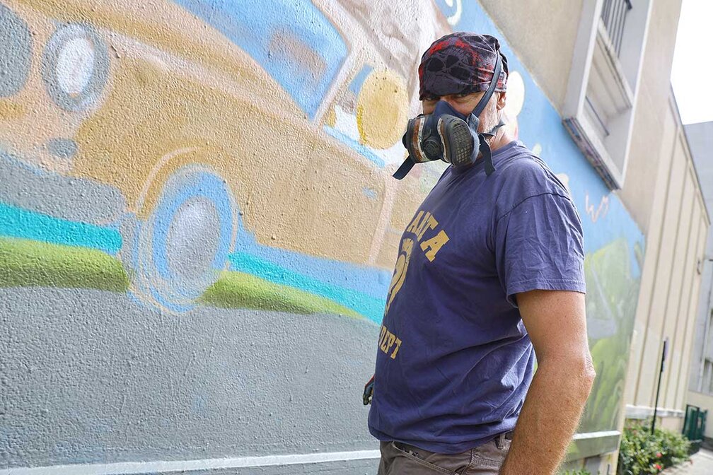 L'artiste Jace en tenue de peintre devant le mur rue Henri Roy à Orléans