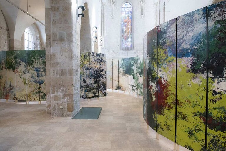 Vue intérieure de la Collégiale Saint-Pierre-le-Puellier à Orléans, montrant des panneaux incurvés recouverts de peintures abstraites aux couleurs vives, installés pour l'exposition de Bruno Desplanques, avec l'architecture médiévale de l'église en arrière-plan.