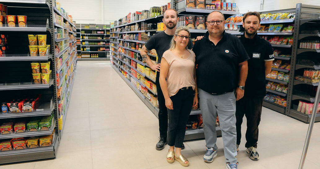 Les membres de la famille posent côte à côte dans un rayon du magasin, entre deux rayonnages remplis de produits.